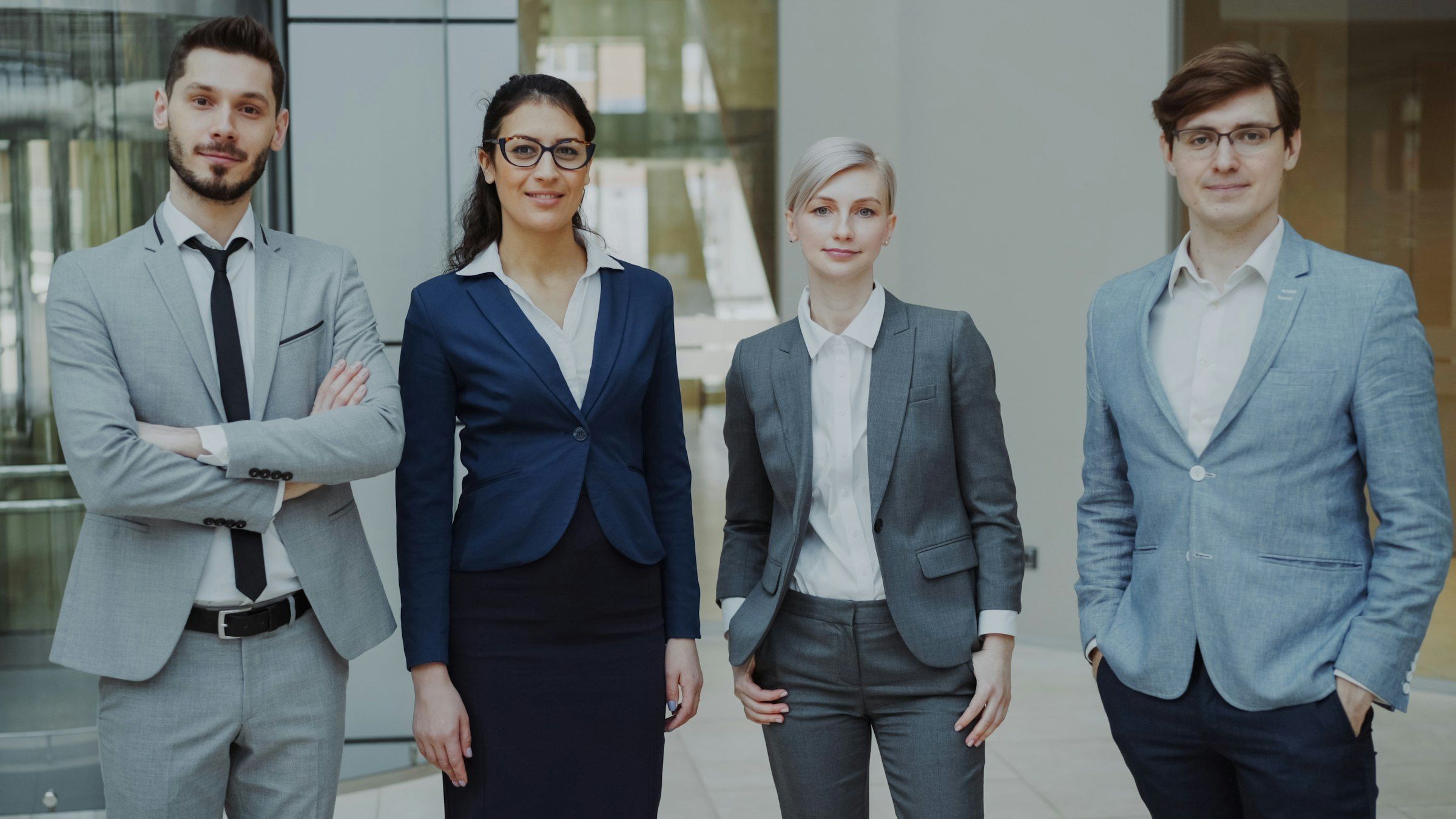 Empat orang berpakaian kerja formal berdiri berdampingan di lobi kantor.